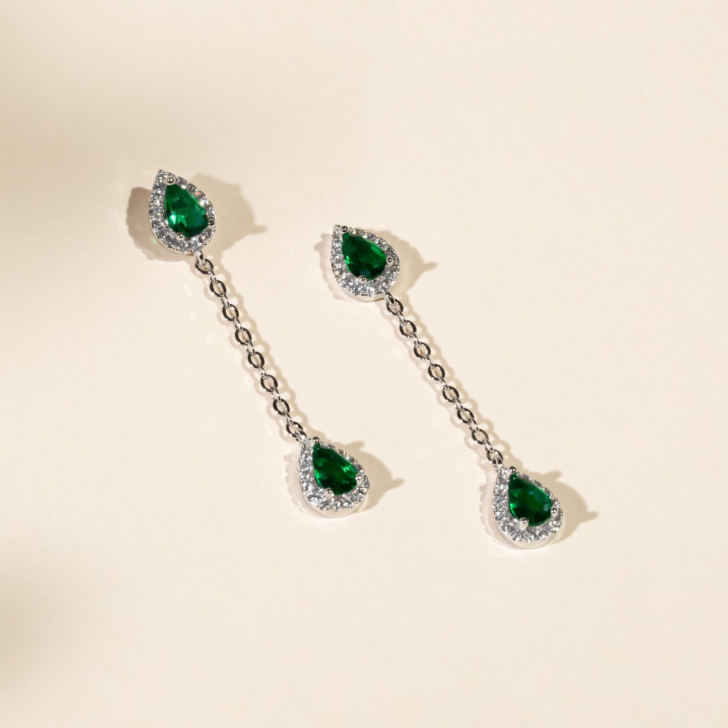 Pair of emerald green gemstone earrings on a beige background