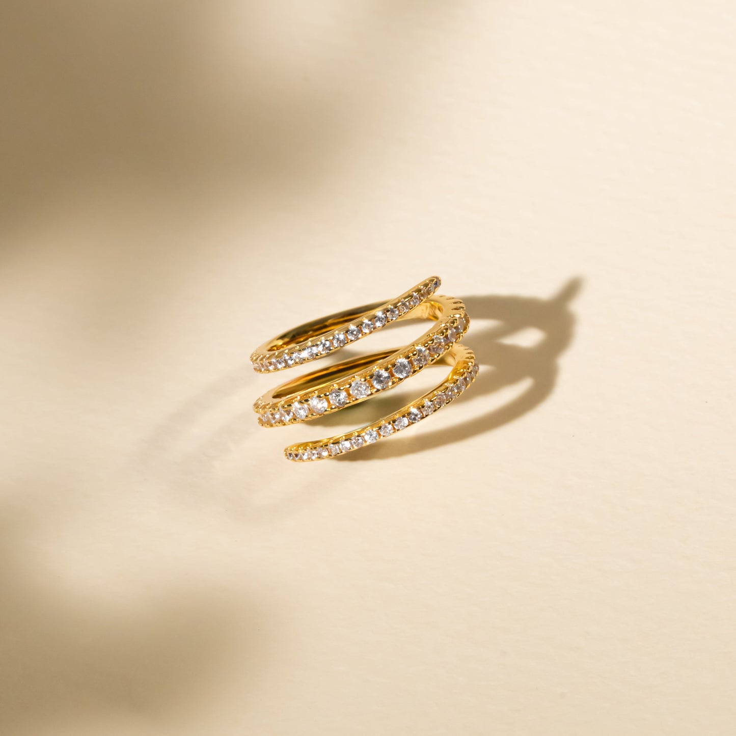 Gold spiral ring with embedded stones on a beige background