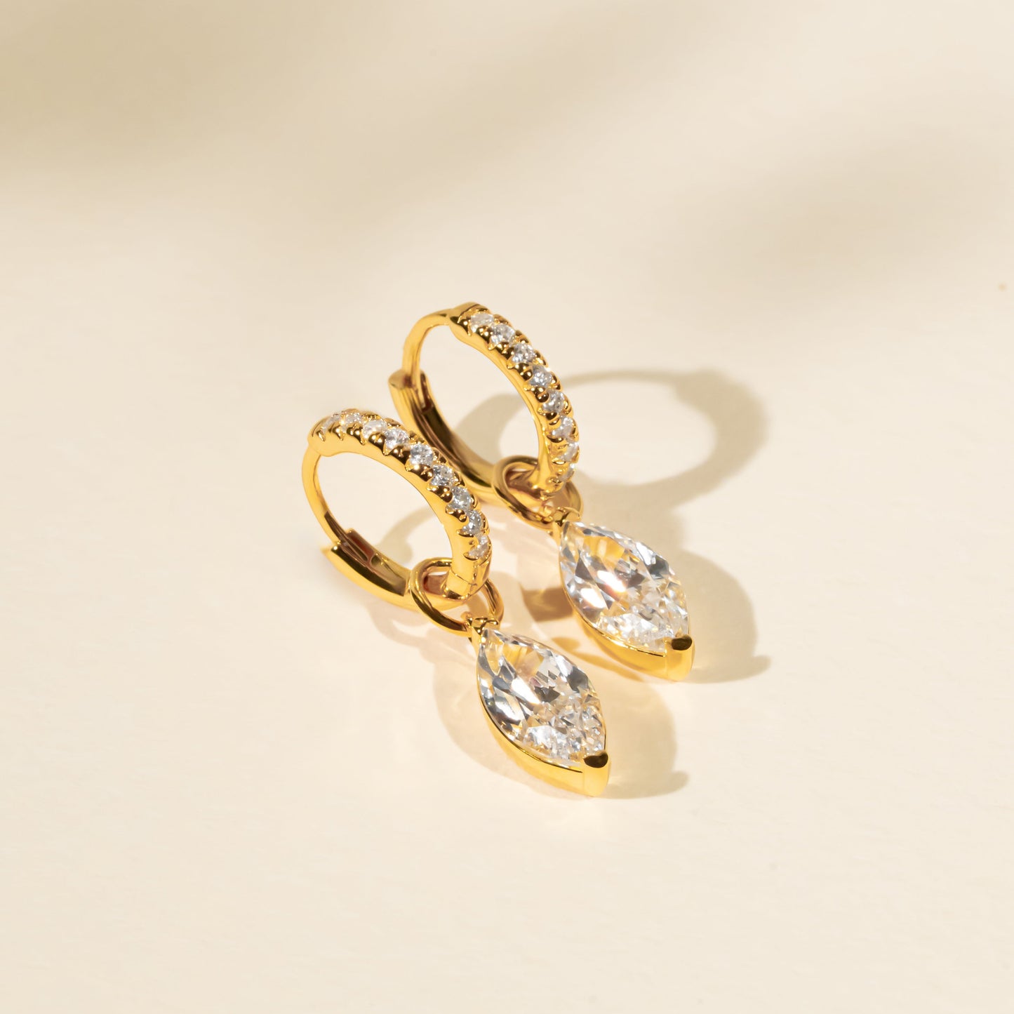 Gold earrings with clear gemstones on a beige background