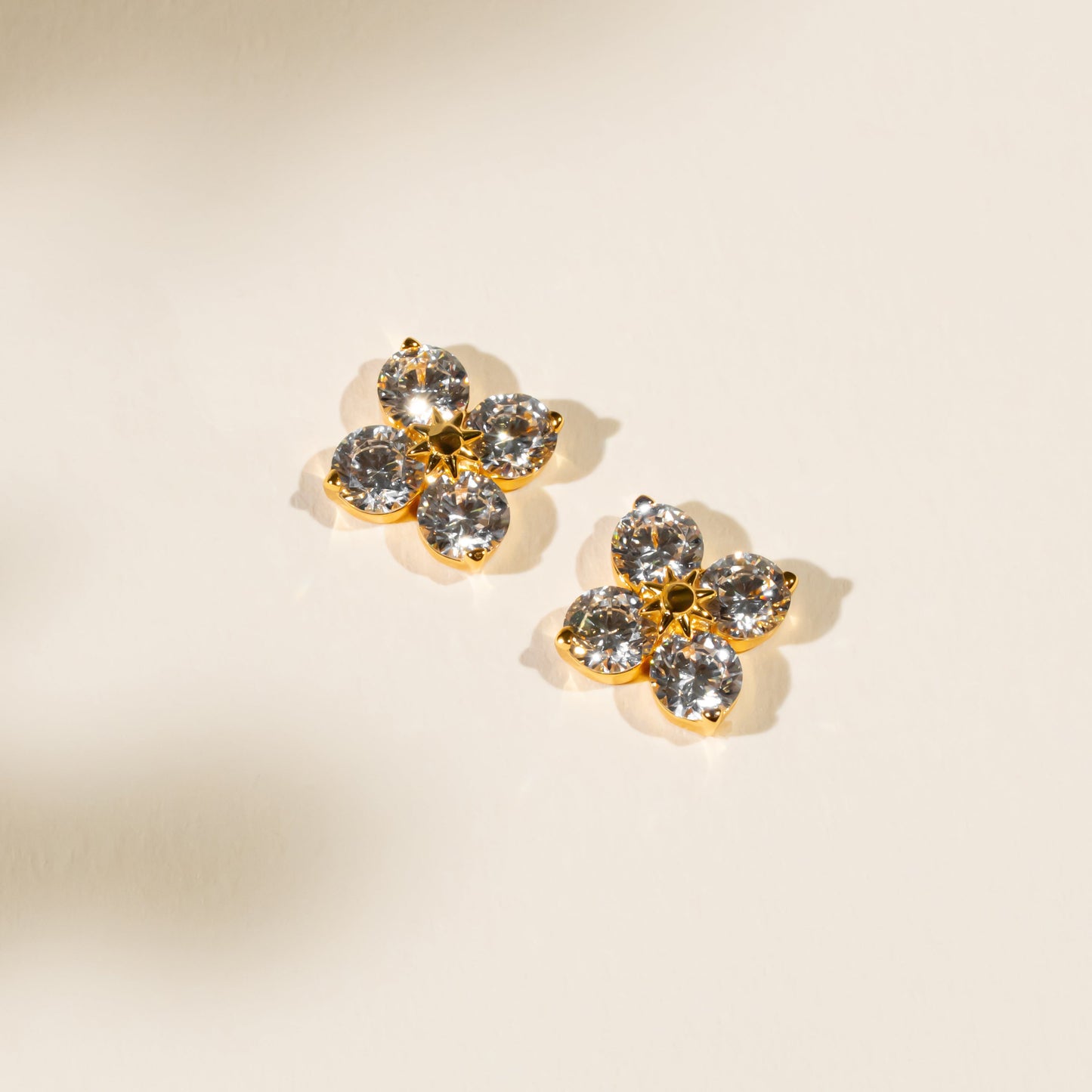 Pair of gold and crystal earrings on a beige background
